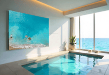 A large minimalist relaxing canvas print of aerial photography of turquoise waters with waves, rocks and sand beach, hanging on the wall of a bright light modern spa room, with Indoor pool, a plant in a pot, and a floor to ceiling windows, looking to ocean.