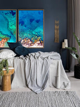 A large coastal wall art canvas set on the wall, over bed, in boho bedroom decor setting. The room features dark gray walls, a light gray woolen carpet, bed surrounded with pillows, plans, a low wooden coffee table and a decorative boho accents. The coastal Aerial wall art canvas set features, rocks, pebbles and turquoise waters, making an relaxing, cosy and calming atmosphere.