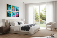 A modern bedroom interior with a bed dressed in white bedding and a dark throw, beneath six colorful abstract framed artworks. A large window with sheer curtains looks out to greenery, and a light upholstered armchair sits beside the window.