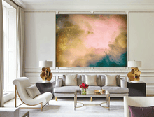 A large abstract wall art print featuring a cosmic nebula design in pink, gold, and teal, displayed in a modern living room setting above a gray sofa.