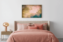 A framed abstract wall art print with soft pink, peach, teal, and gold tones hangs above a neatly made bed with blush pink bedding and pillows in a bright, modern bedroom.