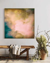 Abstract wall art print featuring a soft blend of pink, gold, teal, and cream tones, displayed in a styled interior above a rustic wooden bench with a draped throw and a potted plant.
