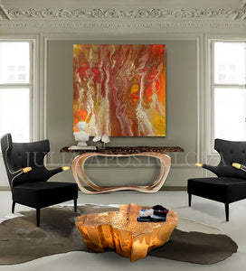 A modern living room featuring two black armchairs with gold accents, positioned around a unique, organic-shaped coffee table made of a golden material. Above the luxury cadenza hangs a large abstract painting with gold, copper, and orange hues. The walls are light-colored, and there are large windows allowing natural light to fill the space