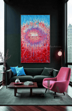 A large vertical abstract wabi sabi painting with a vibrant red, pink, and blue circular design, displayed on a dark wall above a modern living room setup with a black sofa, pink armchair, and coffee table.