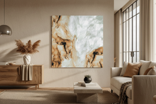 A large square abstract wall art print with flowing earthy tones like ochre clay, cream, tan, brown and soft soulful sage, marbled patterns hangs on a beige wall in a modern living room setting with a sofa, sideboard, and window.