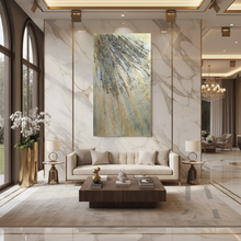 A large vertical abstract sculptured original painting with 3d unique textures with gold, and gray, hangs on a white marble-patterned wall in a modern, luxurious living room with a beige sofa and dark wood coffee table.