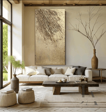 A modern and minimalist living room with neutral-colored furniture, including sofas and a low wooden coffee table . The room features gold abstract artwork on the walls and large windows that let in natural light , creating a serene and calming atmosphere