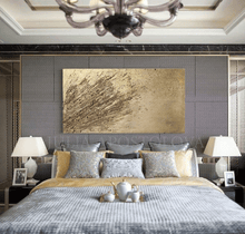 A gold wabi sabi painting with 3d relief gold textures covering the entire canvas. The painting is displayed on the wall of a luxury bedroom with a large window overlooking a natural landscape. The room features a gray bed frame and nightstand, silver decorative pillows, and a coffee service tray , on the bed creating a warm and inviting atmosphere