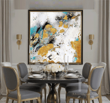 A large framed abstract wall art piece with white, gold leaf, black, and turquoise brushstrokes hangs above a dining table set with chairs in a modern dining room.