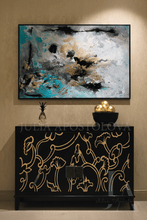 Decorative cabinet with intricate gold designs below a large abstract painting on a beige wall. The painting is painted by artist Julia Apostolova, and framed with black frame.