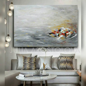 A modern interior space featuring a large abstract minimalist painting with soft gray silver hues, and some gold , white , copper rich textures, Hand-painted by artist Julia Apostolova. The painting is hanging over modern silver couch , and the room has a minimalist design