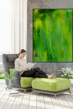 Woman reading a book on a green chair with a large abstract green painting in the background.