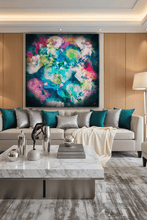 A large abstract canvas painting with vibrant splashes of teal, green, pink, purple, and blue hangs on a light wood-paneled wall above a modern beige sofa with teal and silver pillows in a contemporary living room.