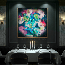 A large framed abstract painting with swirling teal, pink, purple, blue, and cream tones hangs on a dark wall above a set dining table with wine glasses and candles in a dimly lit restaurant interior.