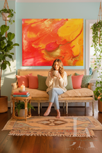 Woman sitting on a couch in a living room with a large colorful orange abstract painting on the wall.