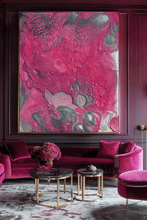 A large abstract wall art piece with swirling magenta, pink, and gray-silver paint textures hangs above a velvet sofa in a richly decorated room with matching pink furniture and dark wood paneling.