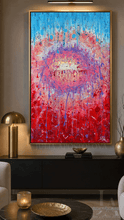 A large framed abstract painting with a vivid red and blue circular composition hangs on a gray wall above a black console table in a modern living room setting.