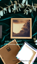 Framed artwork with sunset vintage clouds, on a dark green fabric background with eucalyptus leaves.