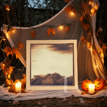 Decorative setup with a framed picture with vintage clouds, surrounded with pumpkins, candles, and string lights in a natural setting. The autumn atmosphere reminded Halloween. 