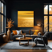 Modern living room with shimmering golden waters abstract wall art, a gray sofa, round wooden coffee table, and large window with autumn foliage.