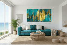 Modern living room with a teal sofa, abstract teal gold artwork, and large windows overlooking the ocean.