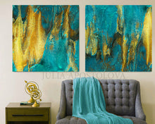 Two abstract paintings with teal and gold tones above a gray sofa with a teal blanket.