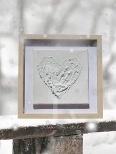 A minimalist white heart-shaped wall art painting on stretched canvas with 3d textures , framed with wooden shadow box frame and displayed on a wooden surface , covered with snow , with white snowy background . Perfect art gift for Christmas, Valentine's Day, Birthday, Anniversary, and any occasion.