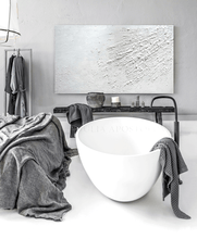 Minimalist bathroom with a white oval bathtub , a gray blanket on the bed , and a white textured painting on the wall in a modern house. The painting is minimalist  with rich white 3d relief textures and the whole room has wabi sabi decor.