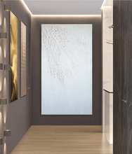 Abstract white painting with rough texture on a white wall in a modern hallway with wooden floor and decorative lighting.