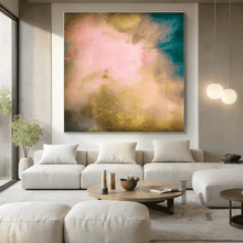A large square abstract wall art print with soft pink, teal, gold, and cream brushstrokes hangs above a light beige sectional sofa in a modern living room.