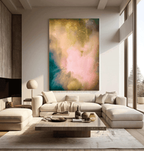 A large abstract canvas print featuring a blend of pink, gold, teal, and cream tones, displayed on a wall above a modern beige sectional sofa in a bright, contemporary living room.