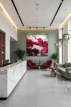 A large abstract wall art print featuring vibrant magenta, pink, sage green, and white brushstrokes, displayed in a modern, bright reception lobby with a marble counter, green sofas, and potted plants.