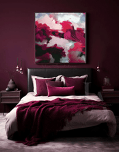 A styled bedroom featuring a large square abstract wall art print with vibrant magenta, pink, sage green, and white brushstrokes, hung above a bed with matching deep burgundy and cream bedding.