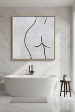 A framed abstract line art of a female silhouette hangs on a marble bathroom wall above a freestanding white bathtub. The artwork features black minimalist lines on a textured light gray and white background with subtle gold flecks, enclosed in a thin gold frame.