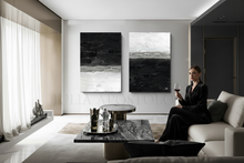 Woman sitting on a couch in a modern living room with abstract art on the wall, with black white and silver colours.