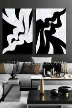 Two abstract black and white artworks on a wall above a modern living room.