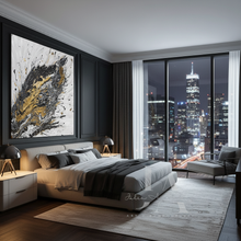 A modern bedroom interior with a large abstract wall art piece above the bed, featuring black, white, and gold brushstrokes. The room has dark gray walls, a bed with neutral-toned bedding, a large window overlooking a city skyline at night, and contemporary furniture.