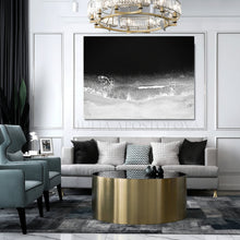 Modern living room with gray sofa, gold coffee table, and framed black white ocean artwork on the wall.