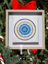 A blue white gold greek evil eye original framed painting in mandala-style . Original artwork in a wooden shadow box frame , blue , gold glitter pattern, surrounded by Christmas decorations including pine branches , candy and a red ribbon.  Ideal art gift for Christmas, birthday, and any occasion.
