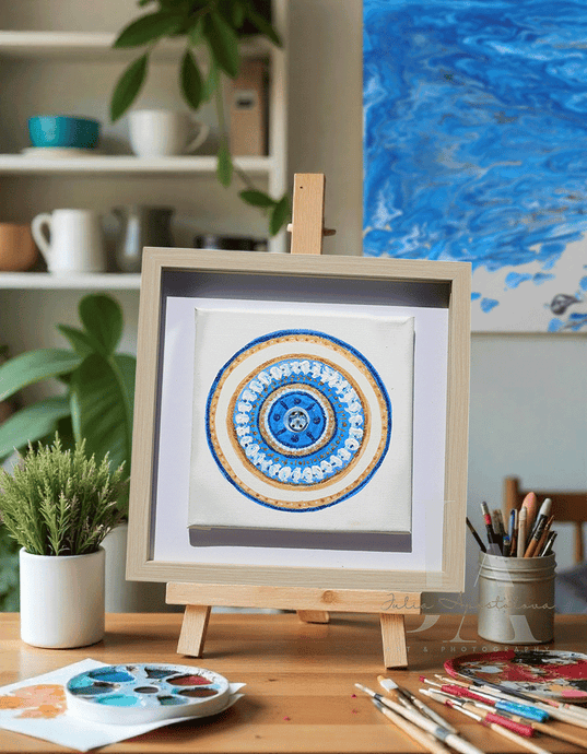 Framed mandala artwork on a wooden easel with art supplies and plants in the background