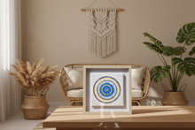 Decorative wall art with a circular design on a wooden table, surrounded by plants and a macrame hanging.