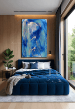 Modern bedroom with blue bedspread, abstract painting, and large window.