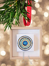 A framed circular mandala artwork with intricate patterns and blue, gold, white colors , surrounded with blurred lights on light beige background.