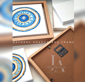 A framed original elegant abstract greek eye painting in circular mandala design with intricate blue and white patterns , along with a wooden frame . NATURAL SHADOW BOX FRAME included with the original canvas glitter painting.  Perfect greek evil eye art gift for protection, for Christmas, Valentine's Day, Birthday, and any occasion.