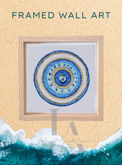 A framed original canvas painting of colorful mandala-like design with concentric circles in shades of blue , white , and gold against a light beige sand beach background and turquoise ocean waves. The painting is like greek evil eye, or nazar, from Turkish, and will be the perfect protection gift for yourself, or someone you love.