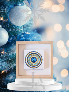 A framed circular mandala artwork with intricate patterns and blue, gold, white colors , surrounded with Christmas tree with blurred lights and ornaments on  light blue background.