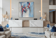 A large vertical abstract canvas painting with blue, white, and dark pink brush strokes hangs on a light beige wall above a marble-and-wood reception desk in a modern lobby setting.