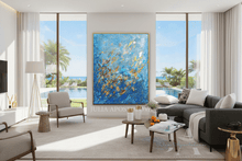 Modern living room with a large blue gold abstract painting, sofa, gold accents, and large windows with gorgeous view to the garden, pool and the ocean.