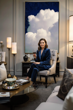 Woman in a blue suit sitting in a stylish living room with a large cloud painting on the wall.