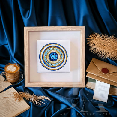 Framed circular artwork with a blue and gold design on a blue fabric background with a cup of coffee and envelope.